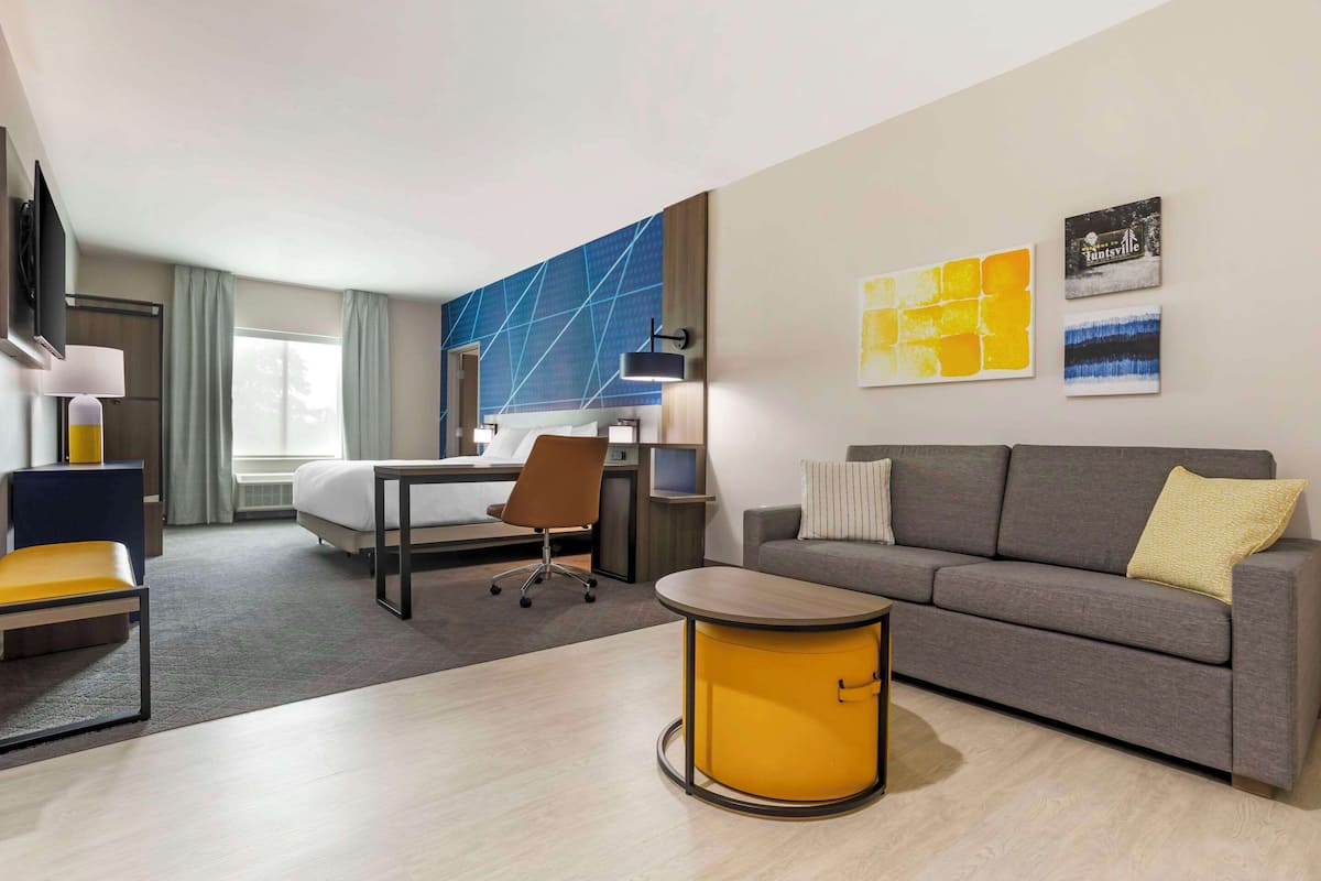 A hotel room with a bed, a desk, a sofa, and a small table.