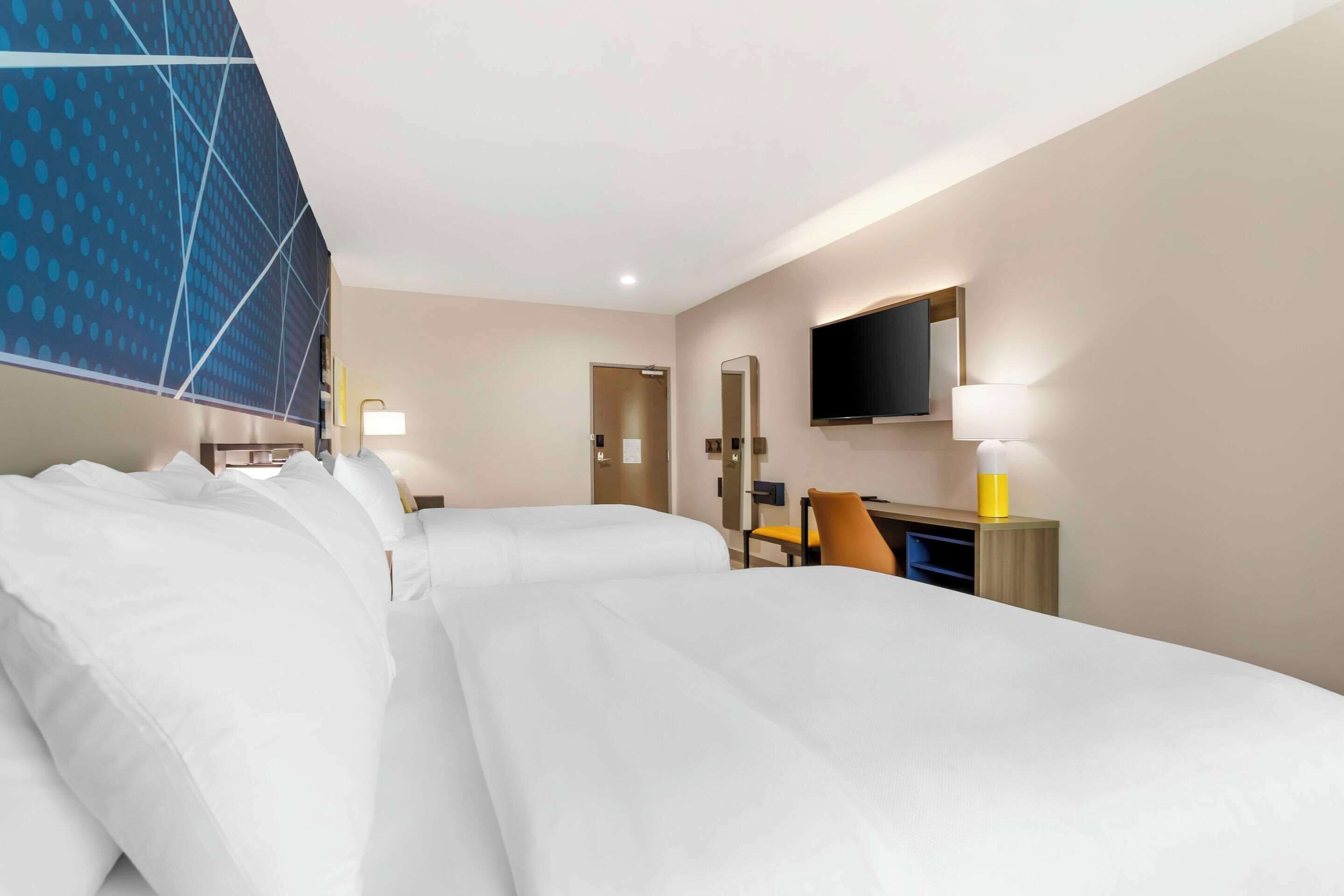 Habitación de hotel con dos camas, un escritorio, una silla, un televisor y un espejo.