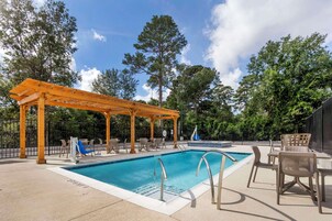 Uma área de piscina com pergolado, espreguiçadeiras e mesa à beira da piscina.