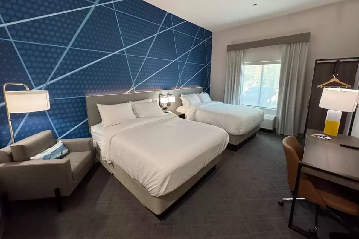 A hotel room with two beds, a sofa, a desk, and a chair.