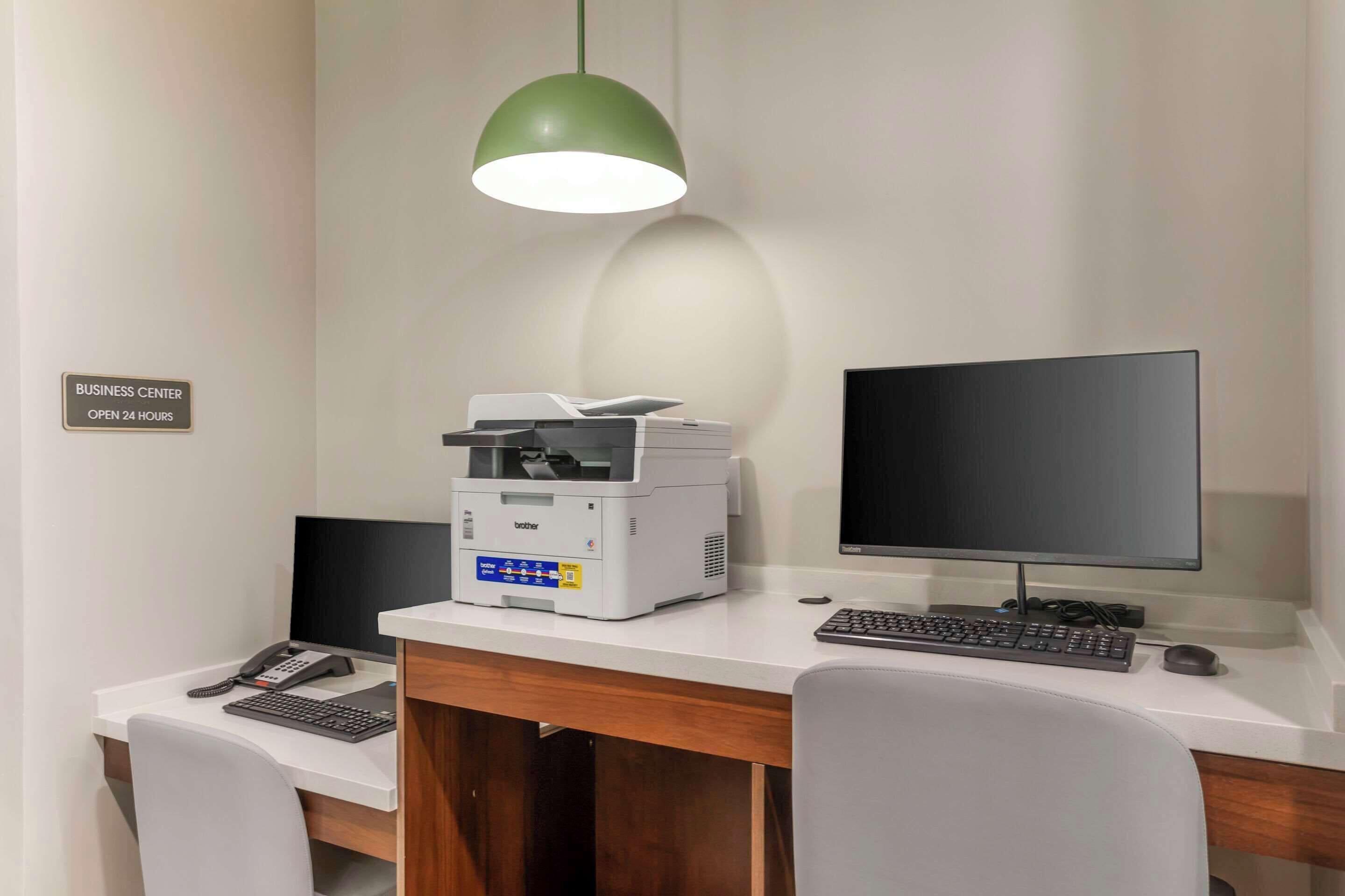 Un centro de negocios con escritorio, impresora, monitor de computadora, teclado y teléfono.