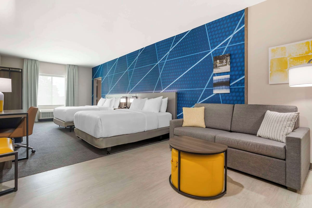 A hotel room with a large bed, a sofa, a small table, and a desk with a chair.
