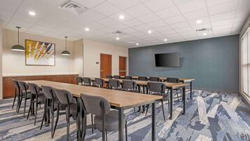 A conference room with a long table, chairs, a mounted TV, and a patterned carpet.
