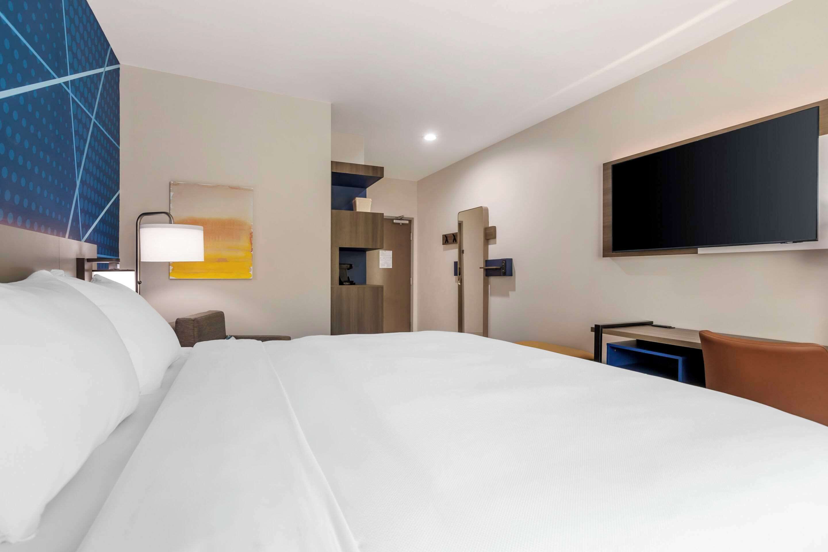 Une chambre d’hôtel avec un grand lit, un bureau, un téléviseur à écran plat et un téléviseur fixé au mur.