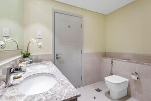 Une salle de bain avec deux lavabos, des toilettes, une douche et une porte.