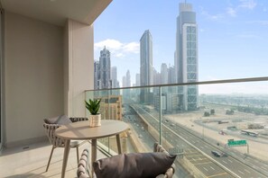 A balcony with a table and chairs, a potted plant, and a cityscape view.