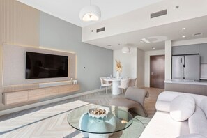 Un salon moderne doté d’un téléviseur à écran plat, d’une table basse en verre, d’un canapé et d’un coin repas avec une table et des chaises blanches.
