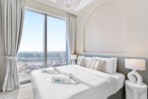 A hotel room with a large window, a bed with white bedding, a bedside lamp, and a view of the cityscape.