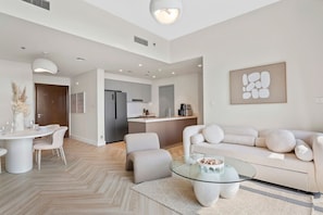 Uma sala de estar moderna com uma mesa de centro de vidro, um sofá e um espaço de jantar com uma mesa e cadeiras brancas.