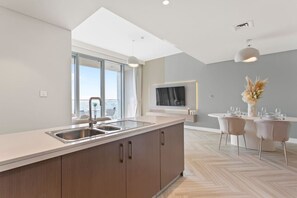 A modern kitchen with a large island, a dining area with a round table, and a large window providing natural light.