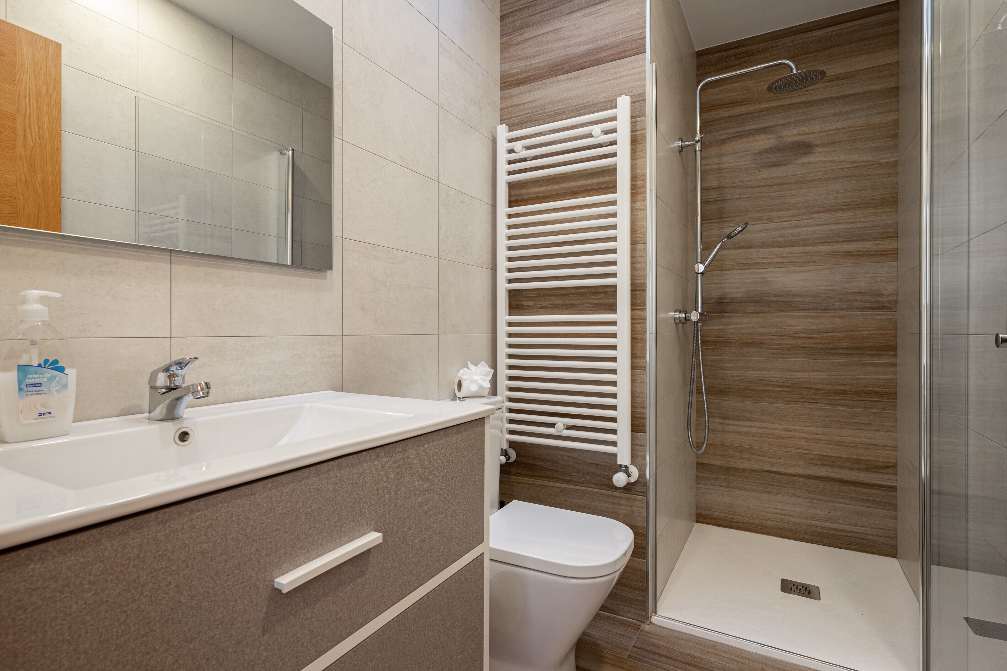 Een badkamer met een wastafel, spiegel, toilet, douche en handdoekhouder.