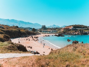 Une plage côtière avec un ciel dégagé, une côte rocheuse et des montagnes à l’horizon.