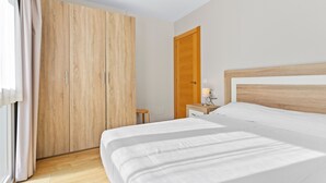 A bedroom with a large wardrobe, a wooden headboard, a bedside table with a lamp, and a window with curtains.