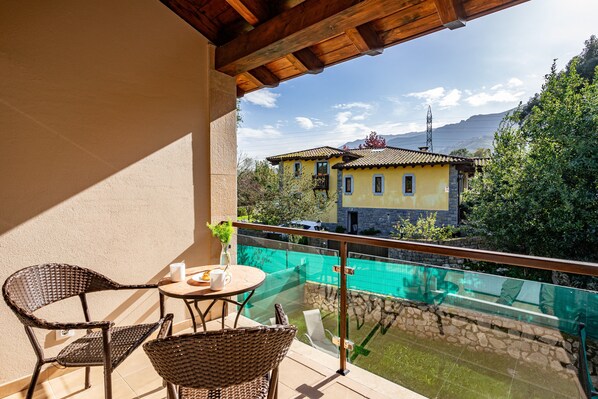 A balcony with wicker furniture, a glass barrier, and a view of a yellow building with a pool. - Apartment '4 Terraza - Antilles Sin Jardin' with Mountain View and Private Terrace (Llanes)