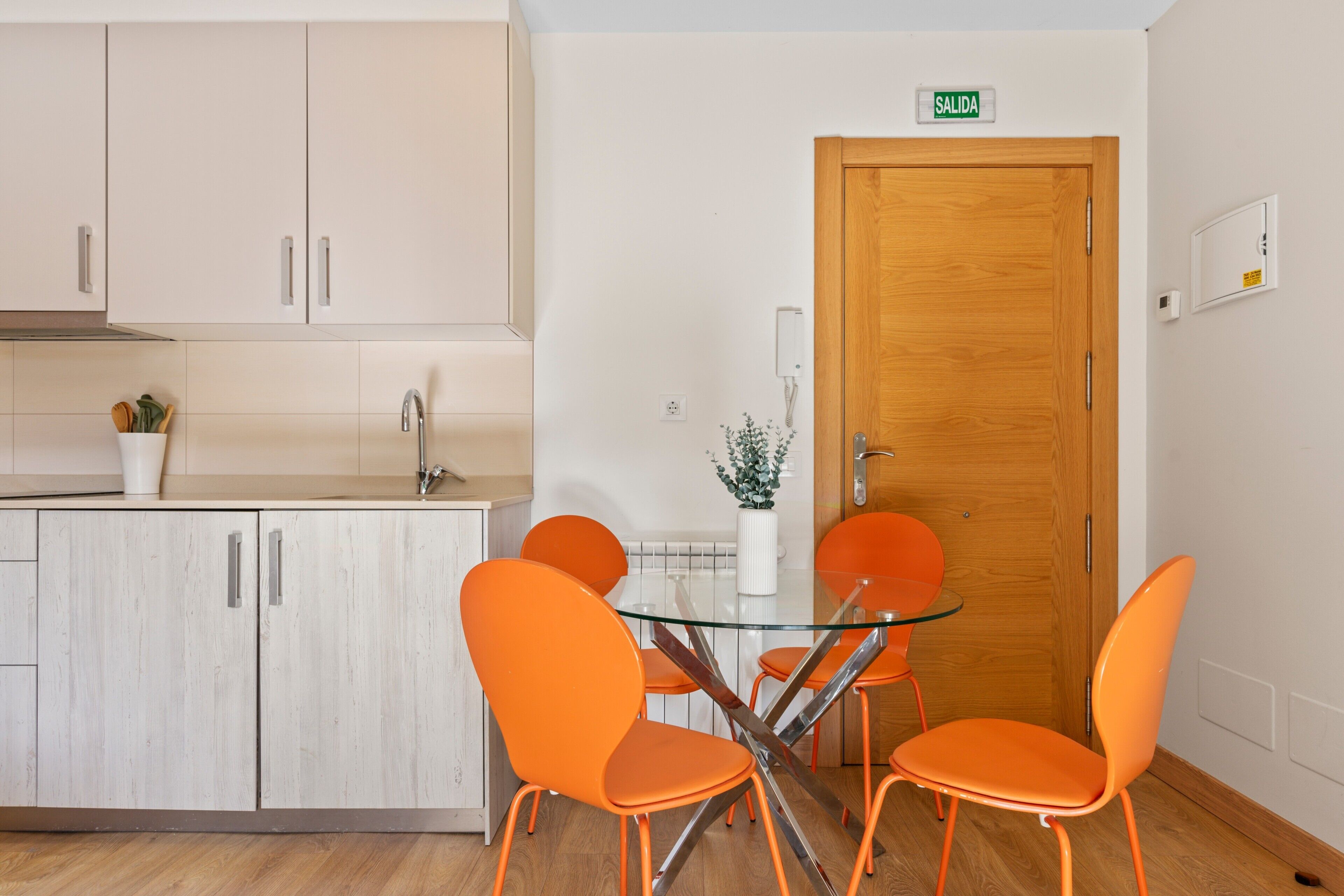 Een moderne keuken met witte kasten, een glazen tafel en oranje stoelen.
