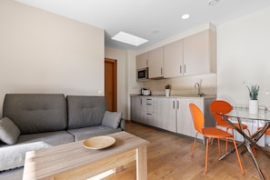 A modern living room with a sofa, a glass dining table, and orange chairs.
