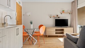Ein modernes Wohnzimmer mit Flachbildfernseher, Holzausbau, orangefarbenen Sesseln und einem grauen Sofa.