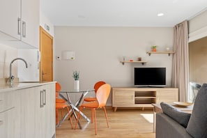 A modern living room with a flat-screen TV, wooden cabinets, orange chairs, and a grey sofa.