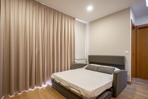 A bedroom with a bed, curtains, a radiator, and a wooden floor.