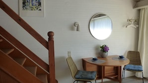 A dining area with a wooden table, two chairs, a round mirror, and a painting on the wall. - Oase in Westerland - 200 Meter zum Strand (Sylt)
