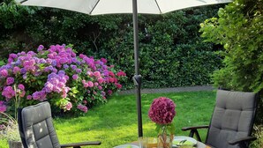 An outdoor dining area with a table set for two, surrounded by chairs, under a large umbrella. - Oase in Westerland - 200 Meter zum Strand (Sylt)