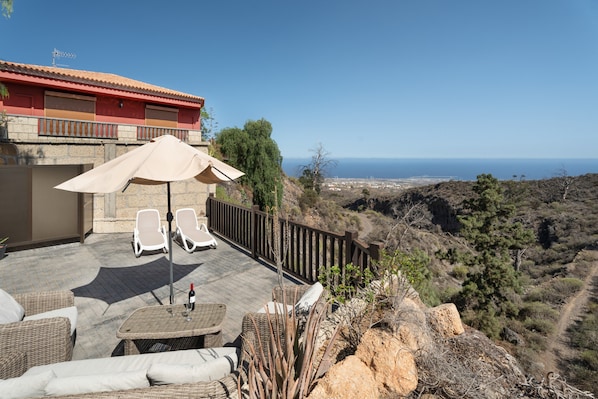 A terrace with wicker furniture, a table with a bottle and glass, and a view of the sea.
