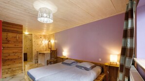 A wooden room with a bed, a chair, a mirror, and a shower area.