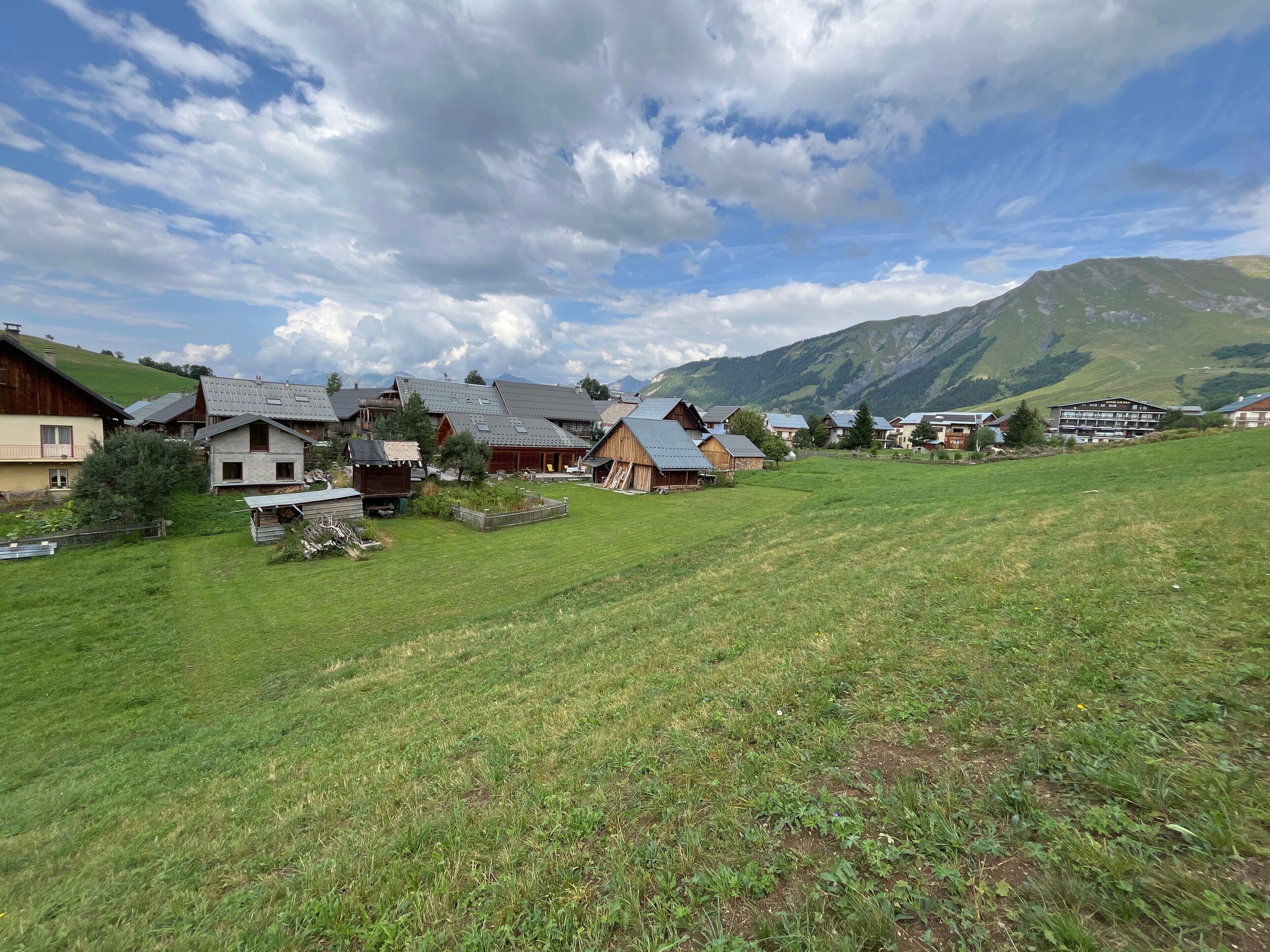 Een landelijk dorp met traditionele huizen, een grasveld en bergen op de achtergrond.