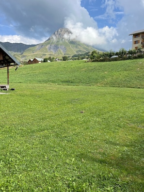 Un campo cubierto de hierba con una montaña al fondo y un edificio de techo inclinado.