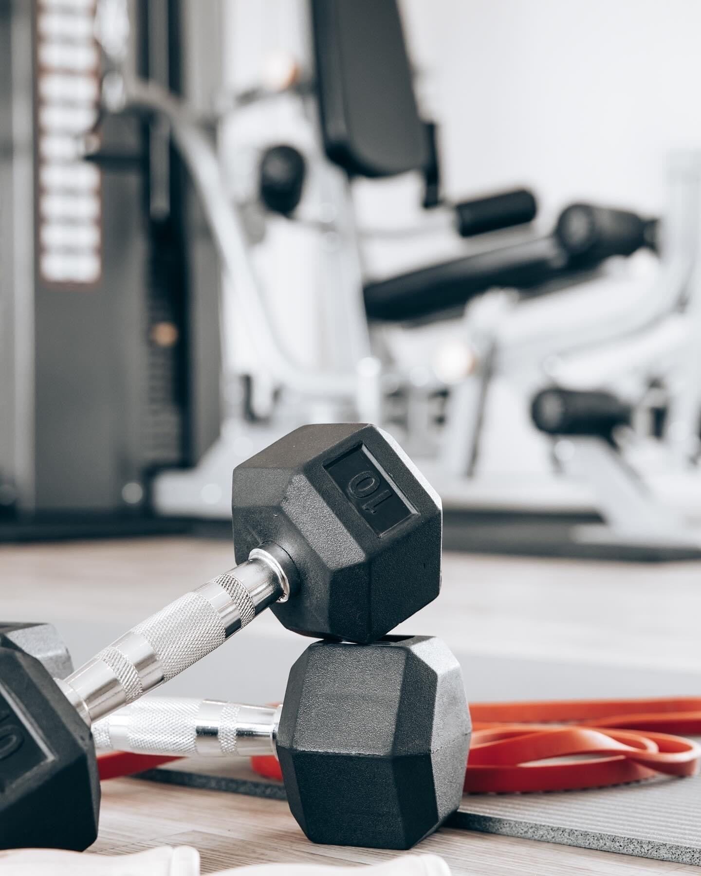 A hexagonal dumbbell with a weight of 10 kg on a wooden floor, with gym equipment in the background.