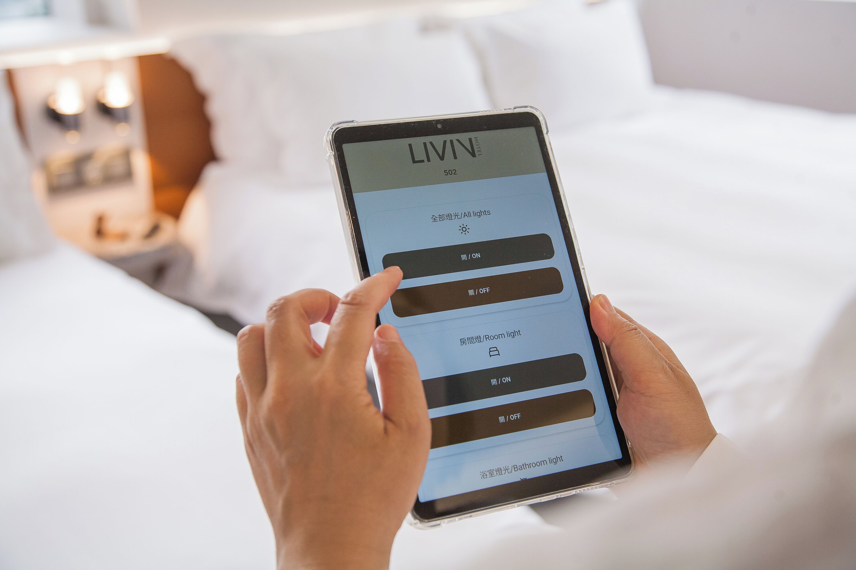 A person holding a smartphone with a hotel app interface displaying room lighting controls.
