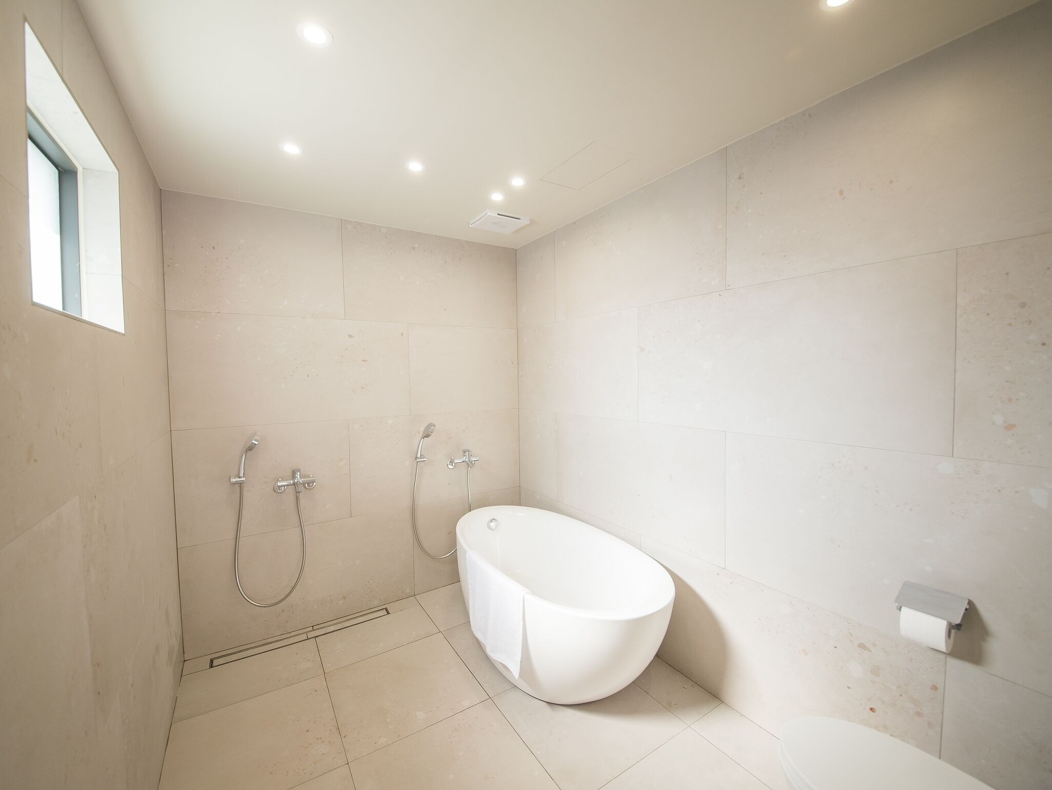 A modern bathroom with a freestanding bathtub, a shower area with two showerheads, and a toilet.