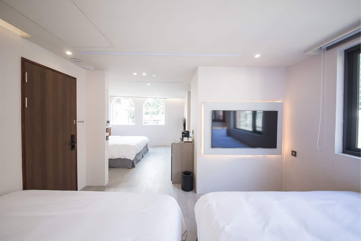 Una habitación de hotel moderna con dos camas, un televisor montado en la pared y un amplio ventanal que proporciona luz natural.
