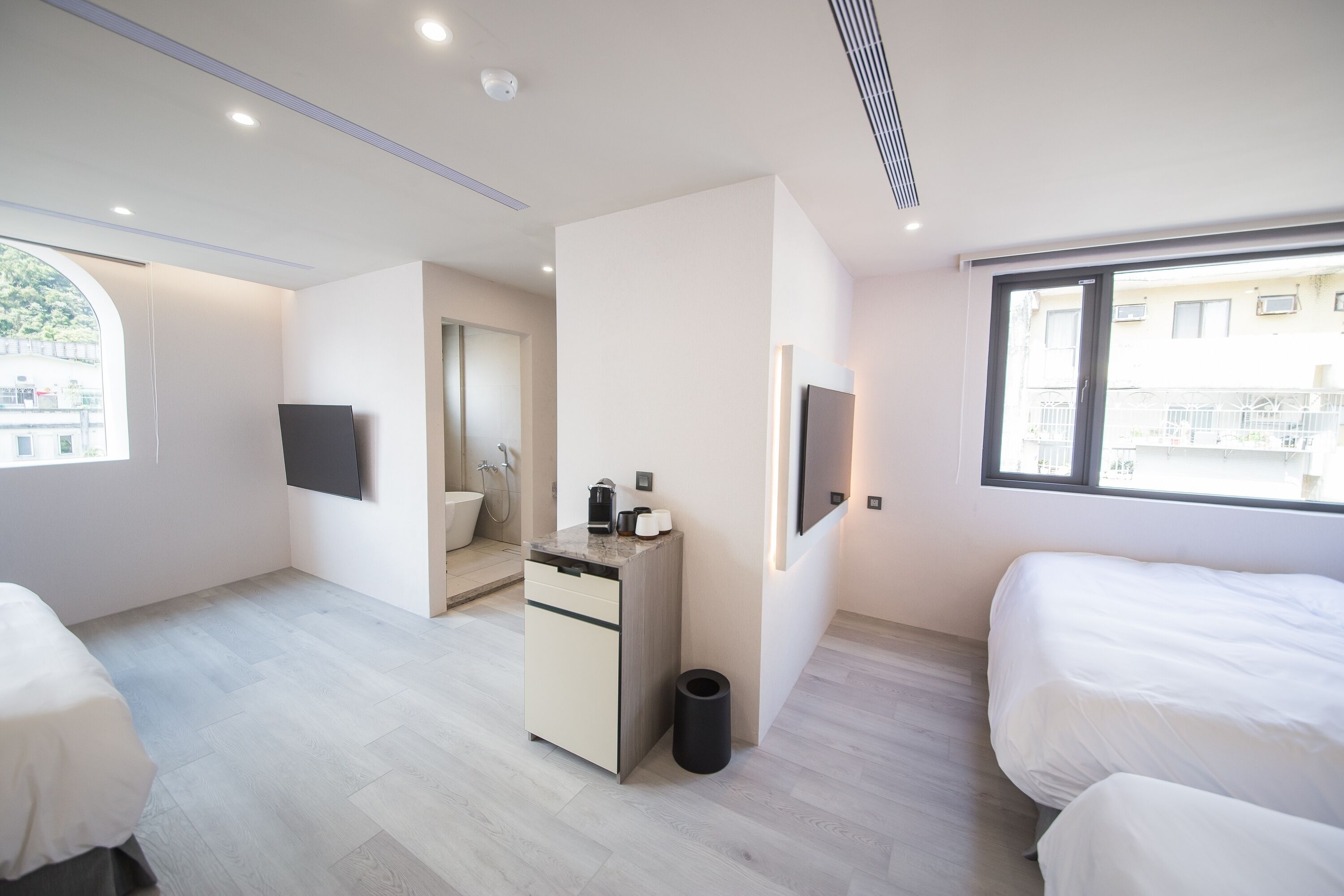 Una habitación de hotel moderna con cama, escritorio con cafetera, televisión y ventana con vistas a edificios.