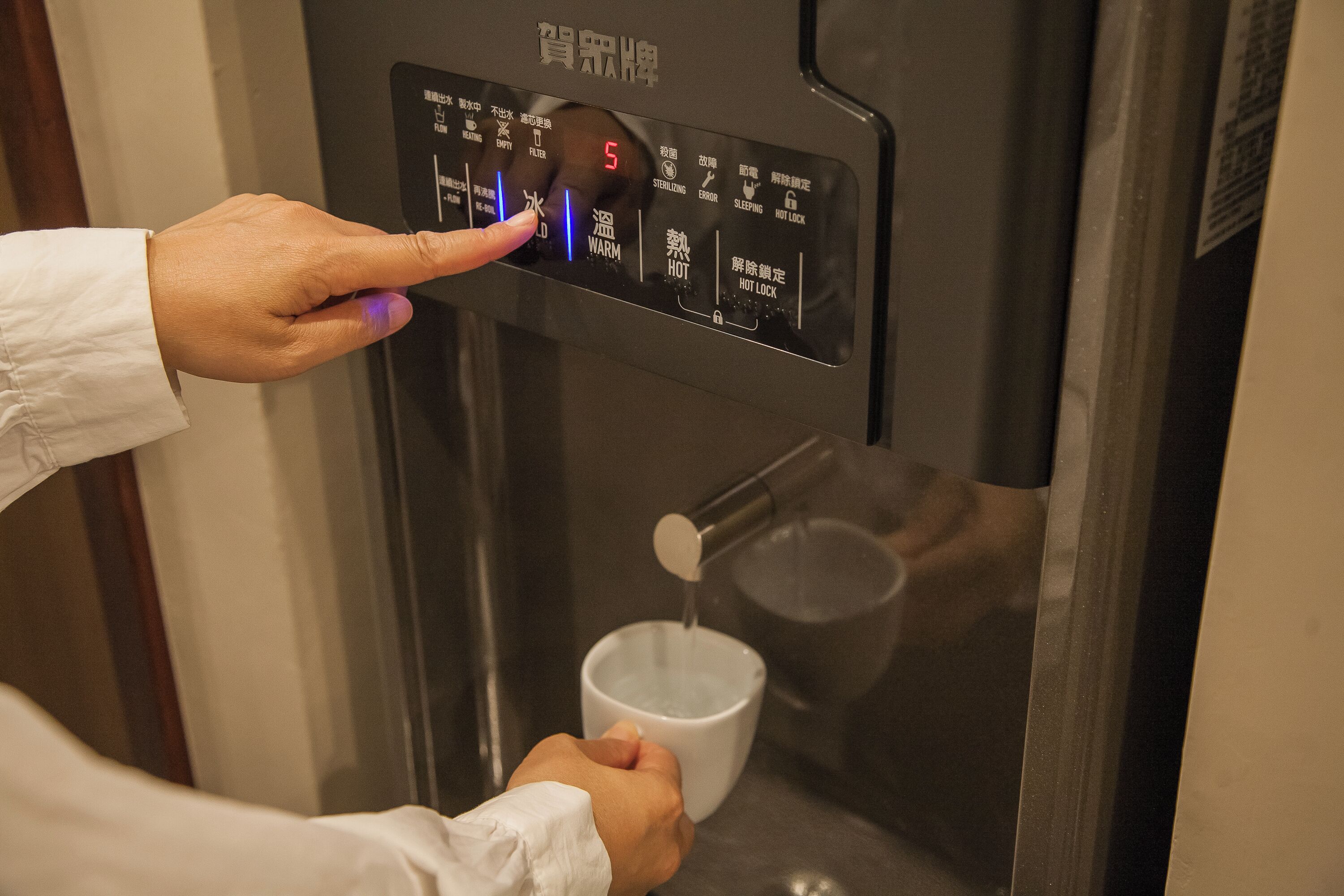 Una mano preme un pulsante su un distributore di acqua con display digitale.