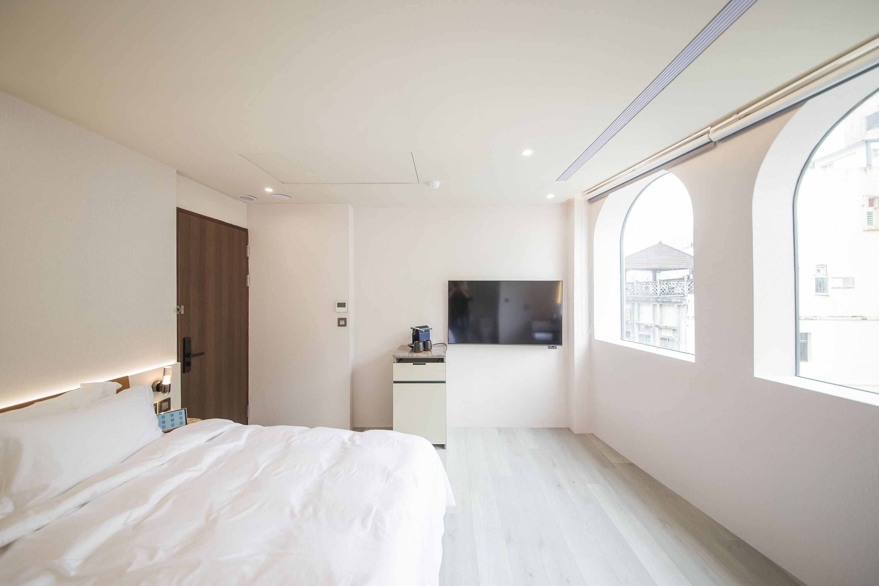 A modern hotel room with a large bed, a desk with a flat-screen TV, and a window with a view of buildings.