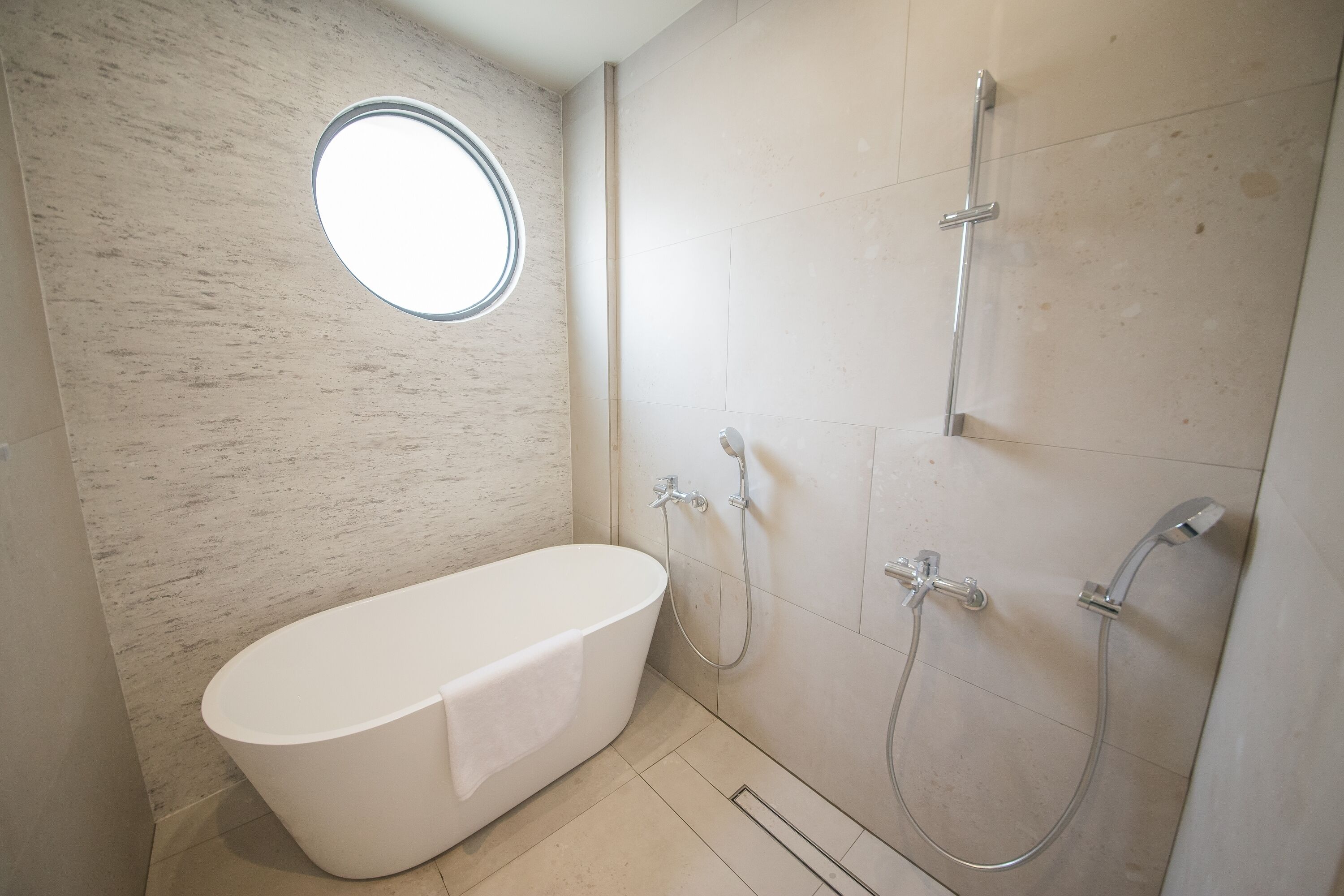 A bathroom with a freestanding bathtub, a shower with a handheld showerhead, and a round window.