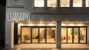Een hotelentree met een modern design, met een groot verlicht bord, glazen deuren en een zitgedeelte met stoelen en tafels.