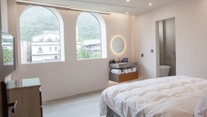 Een moderne hotelkamer met een groot bed, een kaptafel met spiegel en uitzicht op een gebouw door bogenramen.