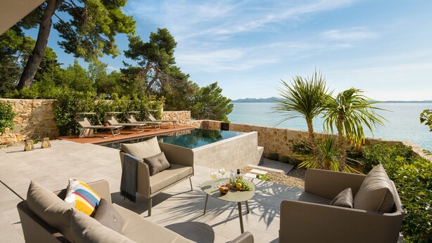 An outdoor seating area with a pool, lounge chairs, and a view of the sea. - Villa Pinea (Zadar)