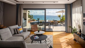 A modern living room with a sofa, coffee table, and a view of the sea through large glass doors. - Villa Pinea (Zadar)