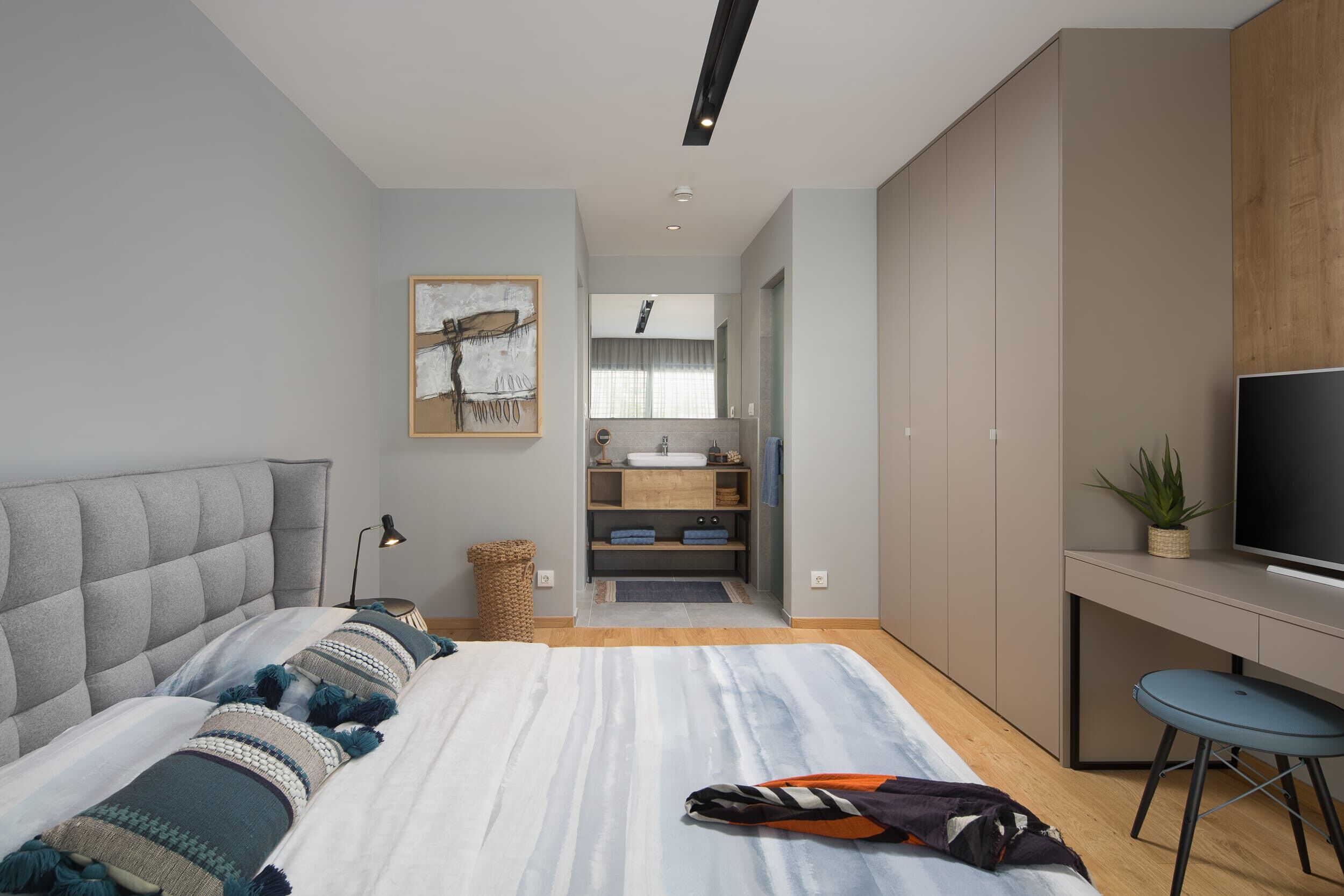 Un dormitorio moderno con una cama grande, un escritorio, un televisor y un baño al fondo.