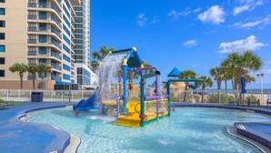 A water park with a water slide and play structures, surrounded by a pool and palm trees. - Horizon Hideaway - Ocean Walk (Daytona Beach)