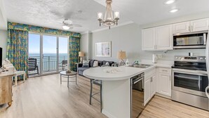A modern kitchen with a central island, white cabinetry, stainless steel appliances, and a view to the outside. - Horizon Hideaway - Ocean Walk (Daytona Beach)
