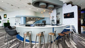 A modern bar area with a curved counter, multiple stools, and pendant lighting. - Horizon Hideaway - Ocean Walk (Daytona Beach)