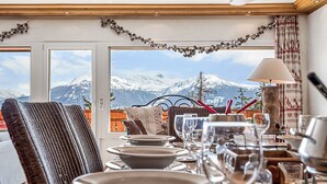 Un comedor con vistas a la montaña, una silla de mimbre, una mesa con platos y vasos, y una lámpara.
