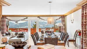 Amplia sala de estar con una mesa de comedor para cuatro personas, un sofá y vistas a montañas nevadas a través de grandes ventanales.