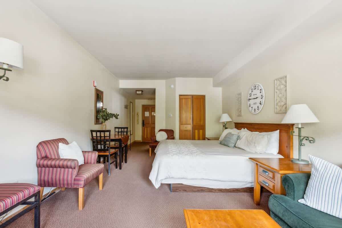 A hotel room with a bed, a desk, a chair, a sofa, and a lamp.