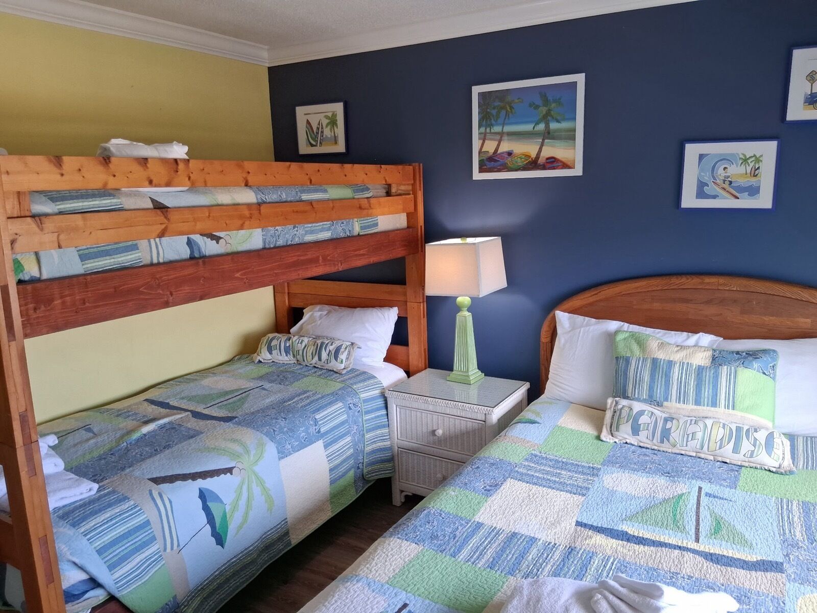 A room with bunk beds, a bedside table with a lamp, and artwork on the walls.