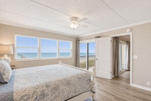 A bedroom with a bed, a ceiling fan, a window with a view of the ocean, and a door leading to a balcony.